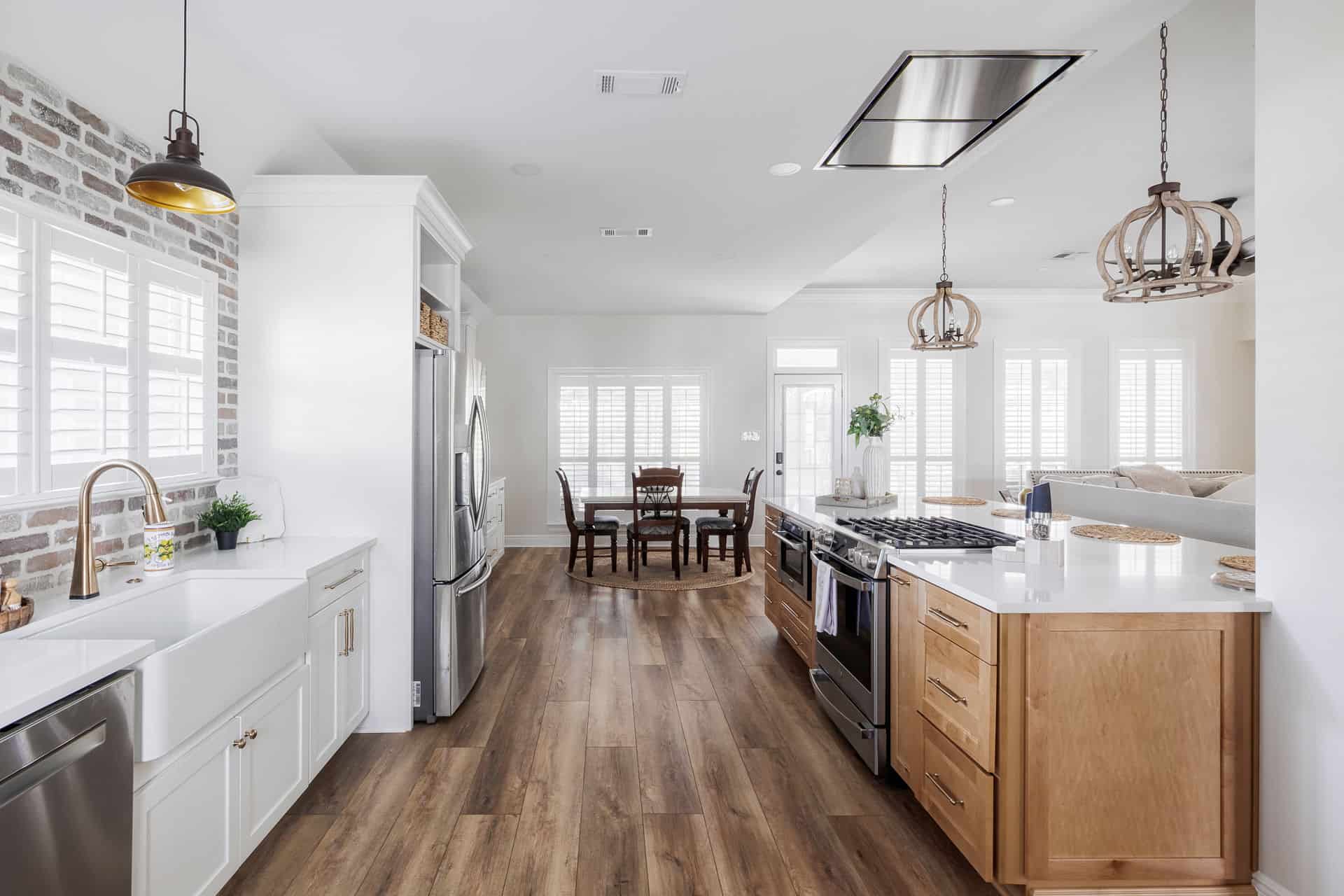 Open-concept kitchen with wood flooring, white cabinets, farmhouse sink, and dining area in the Avalon renovation.