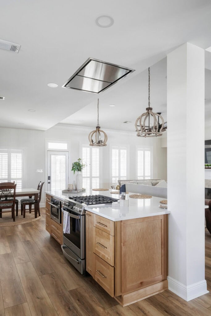 Open-concept kitchen with wood cabinetry, white quartz countertops, recessed lighting, and a flush-mount ceiling hood vent above a center island cooktop.