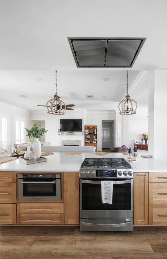 Front view of a modern kitchen island with gas range, built-in microwave drawer, quartz countertops, and a flush-mount ceiling hood vent above.