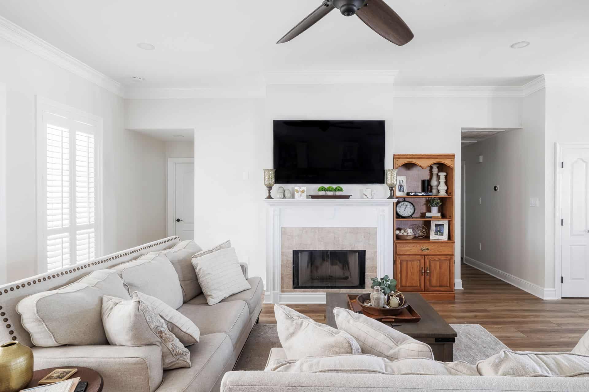 Neutral-toned living room with light sofas, a central fireplace, mounted TV, and natural wood accents in a bright, open-concept home.