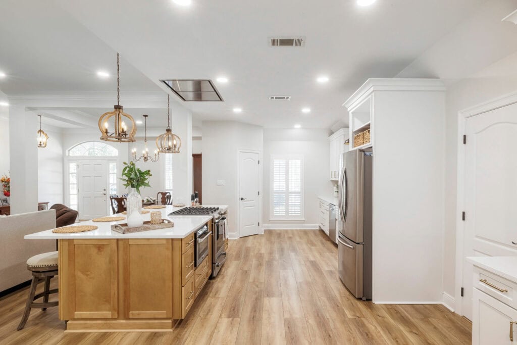 Open-concept kitchen with large island, white cabinetry, wood floors, and pendant lighting