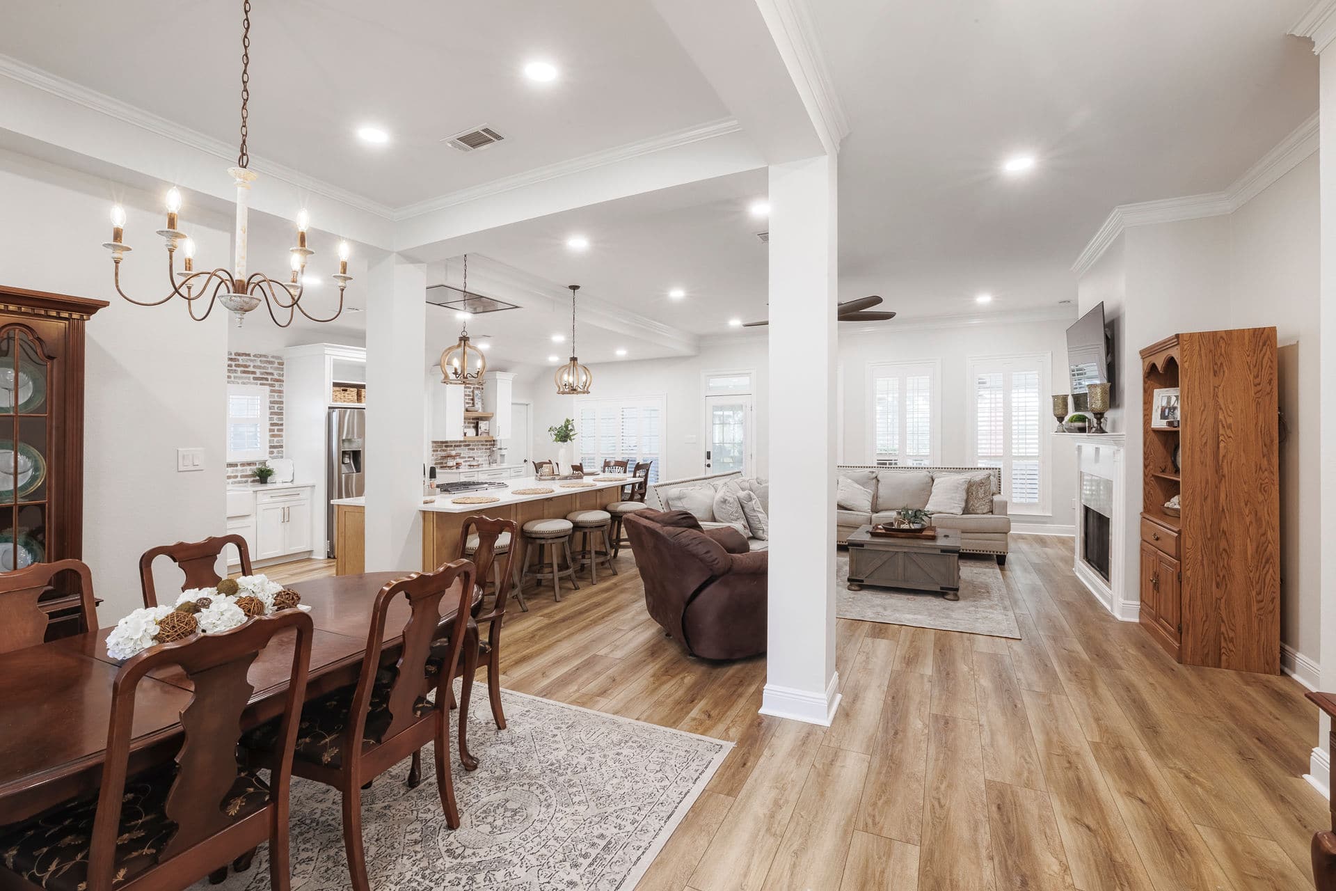 Open-concept kitchen, dining, and living area featuring wood flooring, recessed lighting, custom island with seating, and cohesive transitional design.