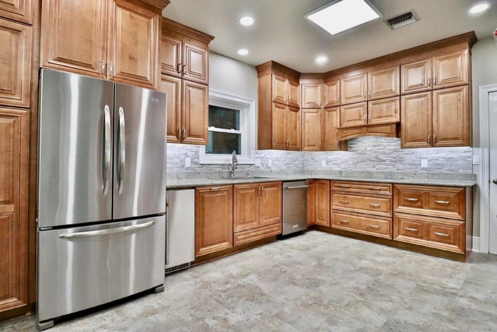 Spacious kitchen with natural wood cabinetry, stainless steel appliances, and a gray stacked stone backsplash.