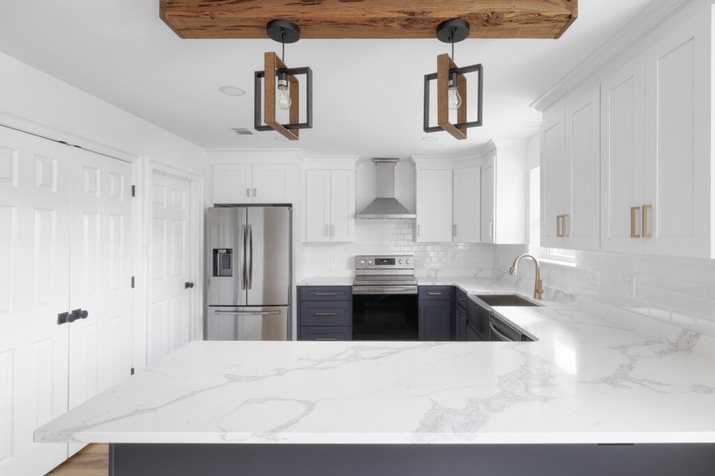 Bright two-tone kitchen with quartz countertops, white upper and navy lower cabinets, stainless appliances, and decorative pendant lighting on a wood beam.