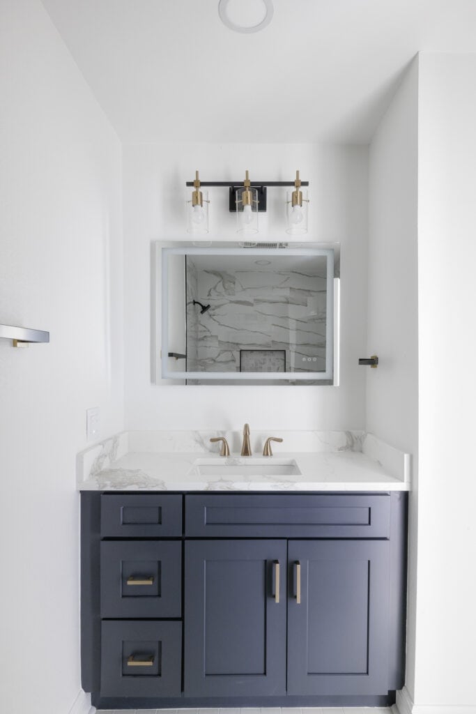 Navy blue bathroom vanity with marble countertop, gold faucet, and LED mirror.