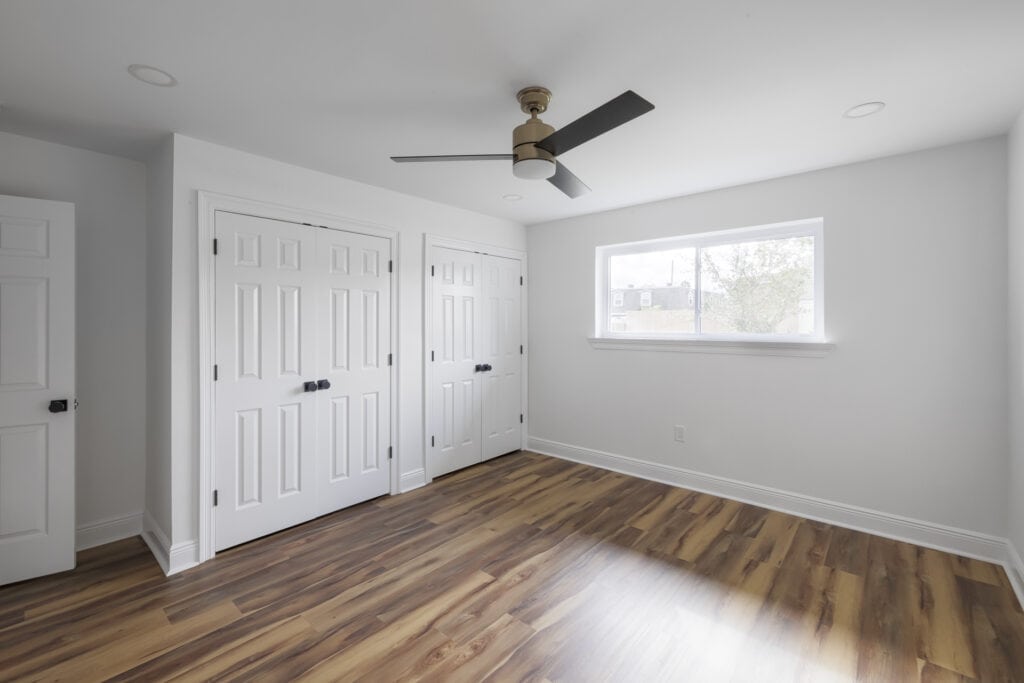 Modern bedroom with double closets, wood-look floors, and a contemporary ceiling fan.