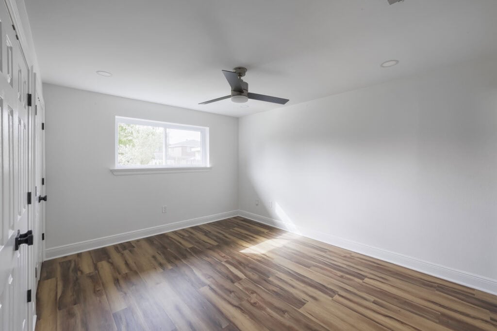 Remodeled bedroom with wide-plank wood-look flooring, white walls, and modern ceiling fan.