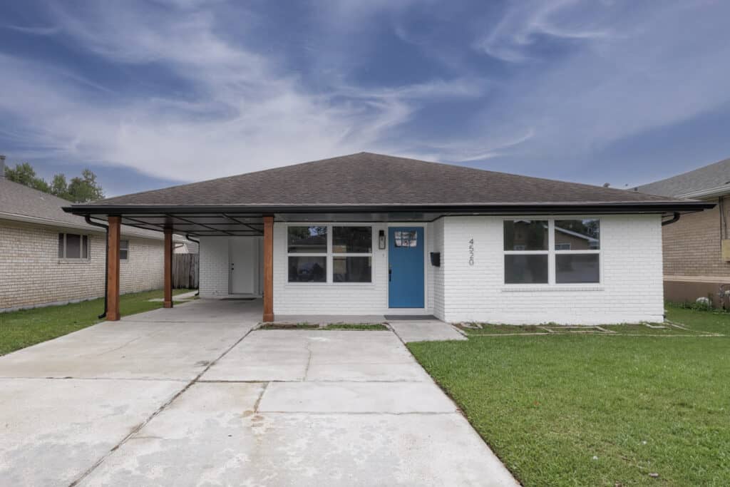Modern white brick home with carport, blue front door, and wood post accents.