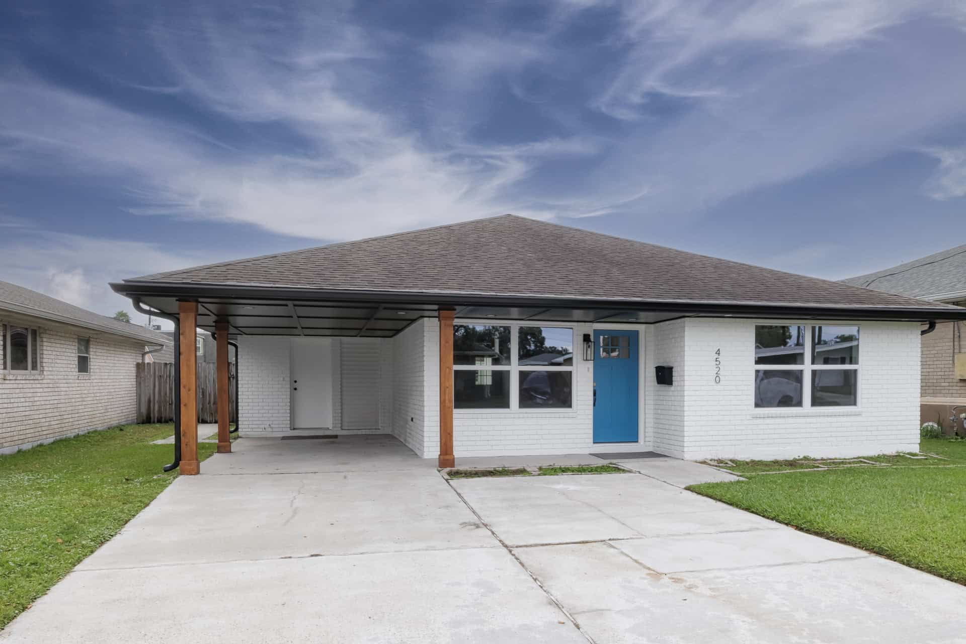 Modern exterior renovation with white painted brick, bold blue door, wood posts, and a streamlined carport.