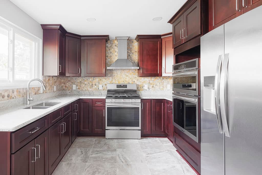 Kitchen with cherry wood cabinets, stainless steel appliances, granite countertops, and a natural stone backsplash.