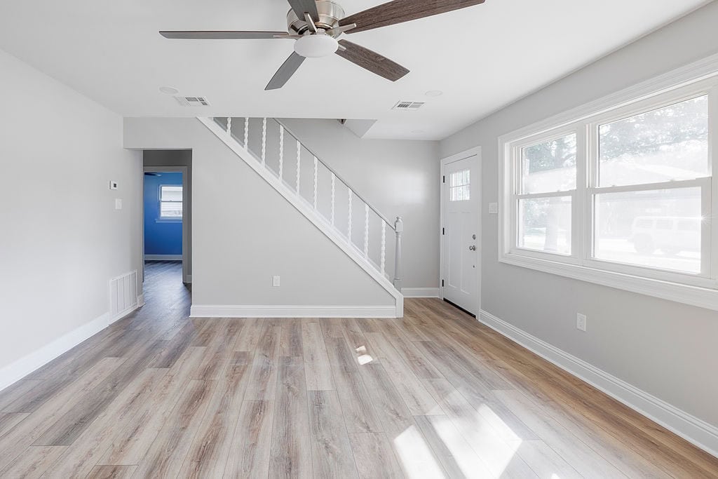 Bright living space with new wood-look flooring, neutral paint, a modern ceiling fan, and updated staircase from the Hester renovation project.