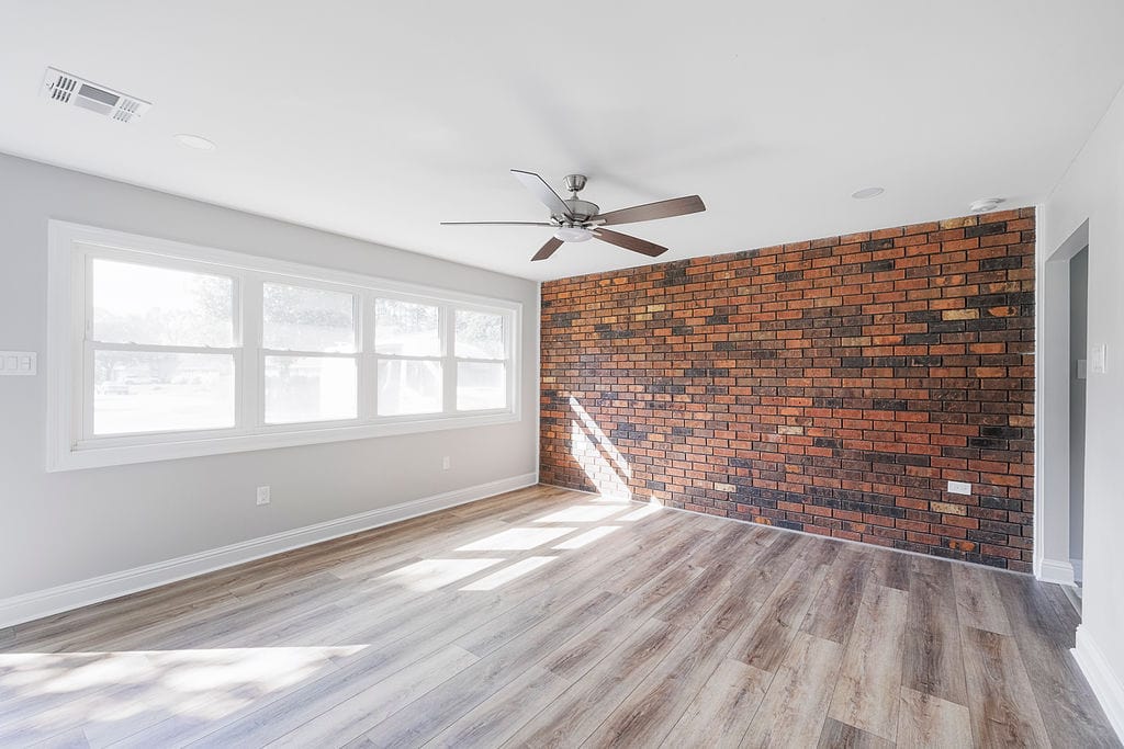 Bright living room with full-length windows, exposed brick wall, and wood-look flooring