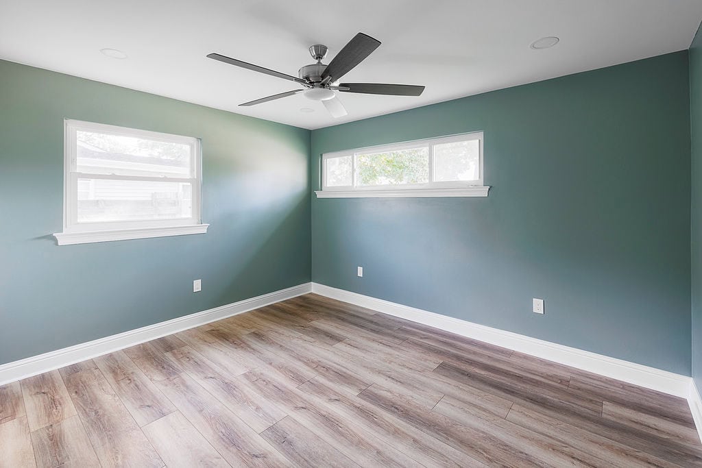 Spacious green bedroom with wood-look floors and large windows