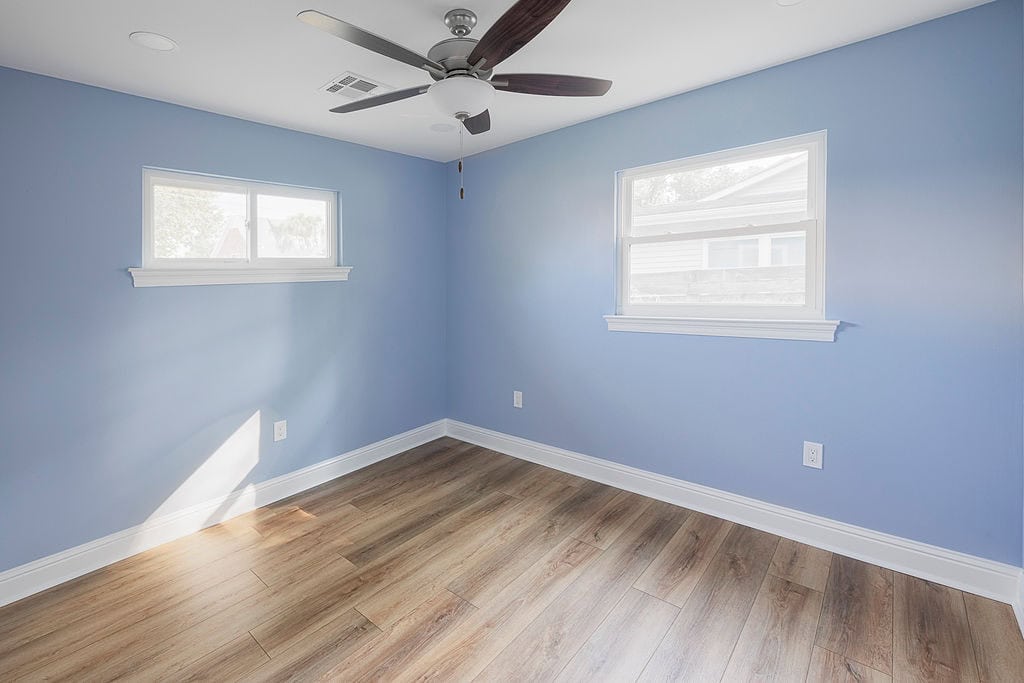 Bright renovated bedroom with two windows, blue walls, and wood-look flooring