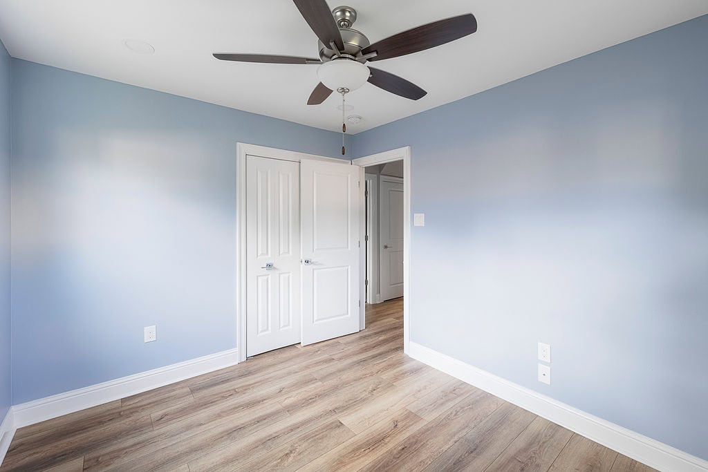 Renovated bedroom with light blue walls, wood-look flooring, and modern ceiling fan