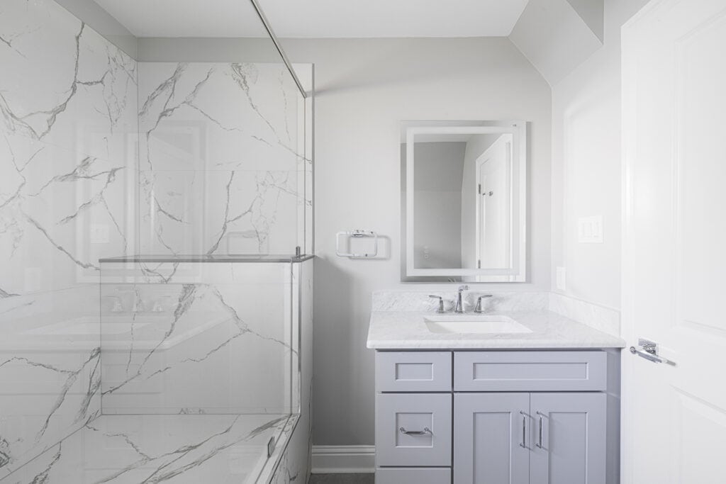 Modern bathroom renovation with a marble-look shower, light gray vanity, and clean white finishes in the Hester project.