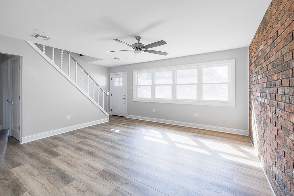 Bright living room with brick accent wall, wood-look flooring, and staircase