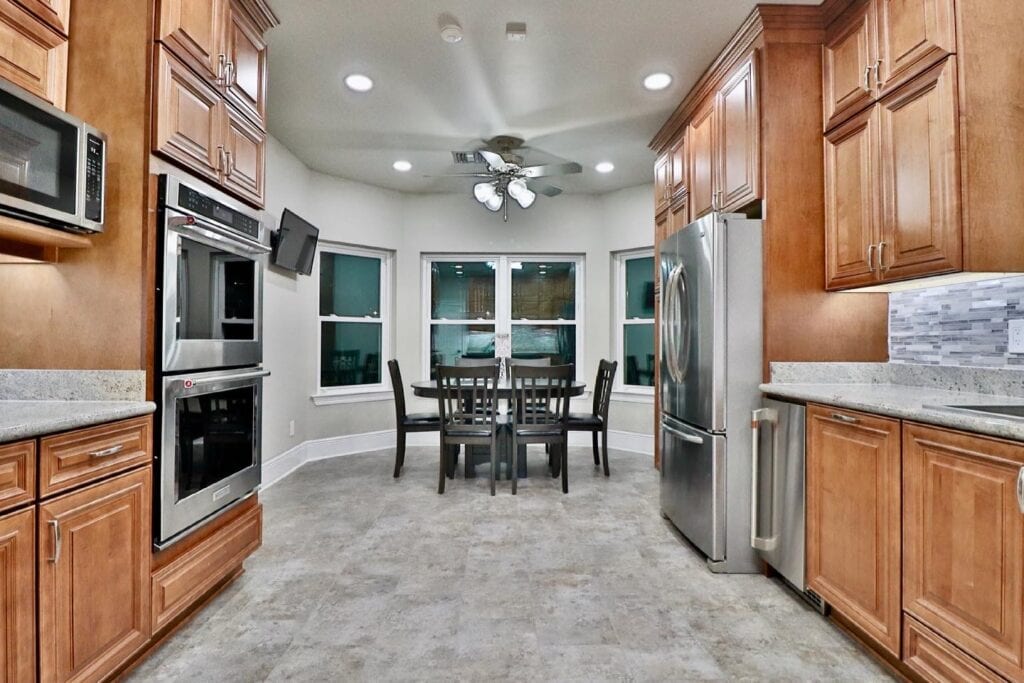 Spacious kitchen with dining nook, natural wood cabinets, stainless steel double oven, and a ceiling fan.