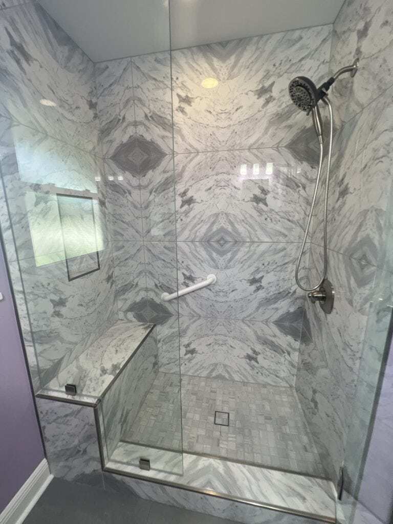 Marble-tiled walk-in shower with built-in bench, niche, and handheld showerhead.