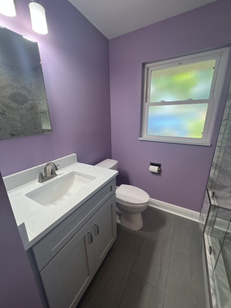 Lavender-painted bathroom with single vanity, white quartz top, and glass shower enclosure.