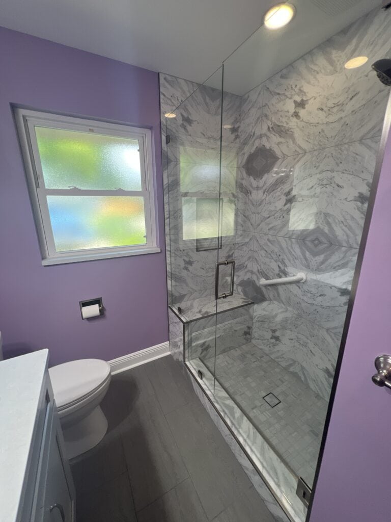 Tight-layout bathroom with glass walk-in shower, marble tile, and lavender-painted walls.