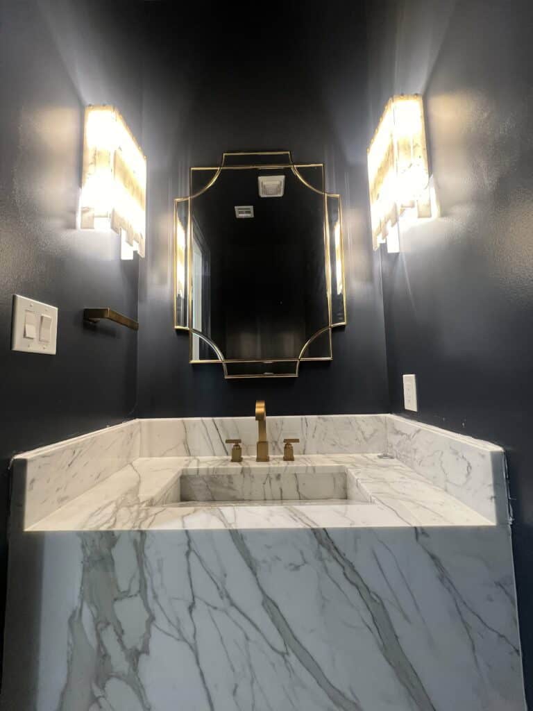 Luxurious powder room with marble waterfall sink, gold fixtures, and dark navy walls
