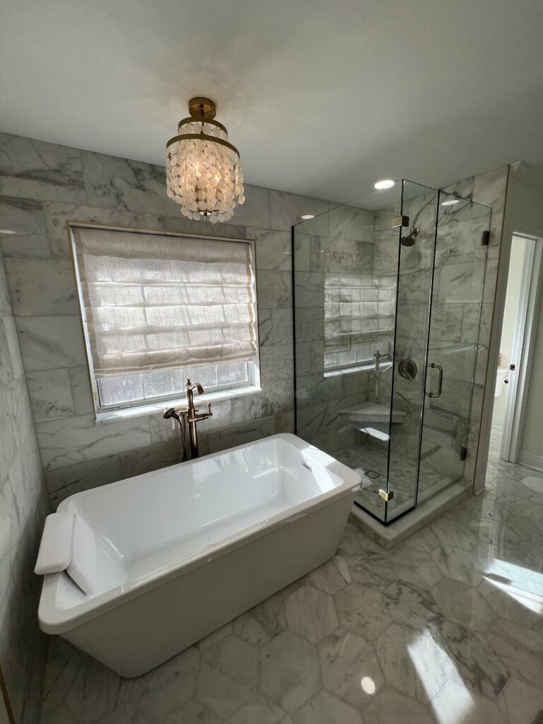 Freestanding bathtub and marble shower under chandelier lighting