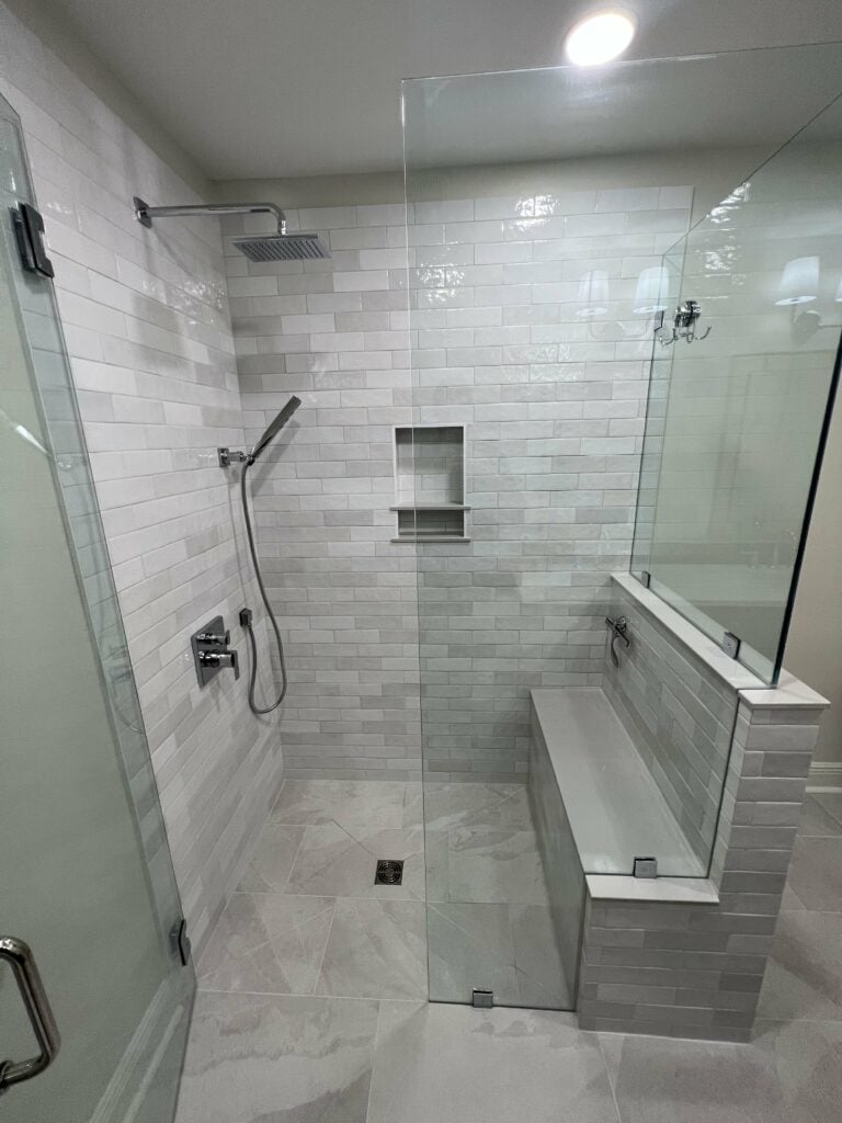 Curbless walk-in shower with large bench, white subway tile, and frameless glass enclosure