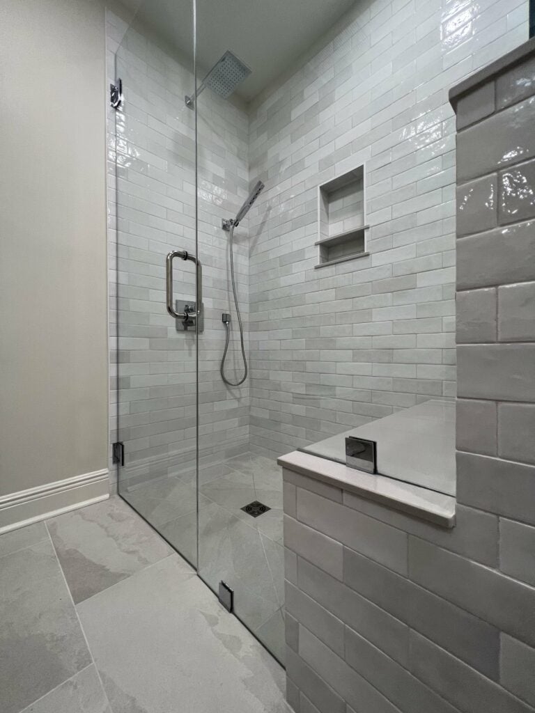 Custom tiled walk-in shower with glass door, handheld sprayer, and built-in shower niche