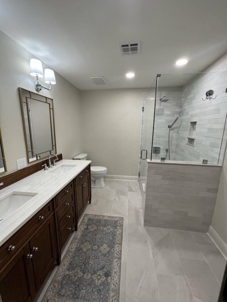 Modern double vanity bathroom with glass shower and large tile floors.
