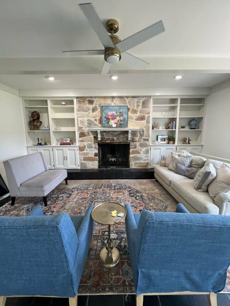Living room with stone fireplace, built-in shelving, blue chairs, and neutral seating.