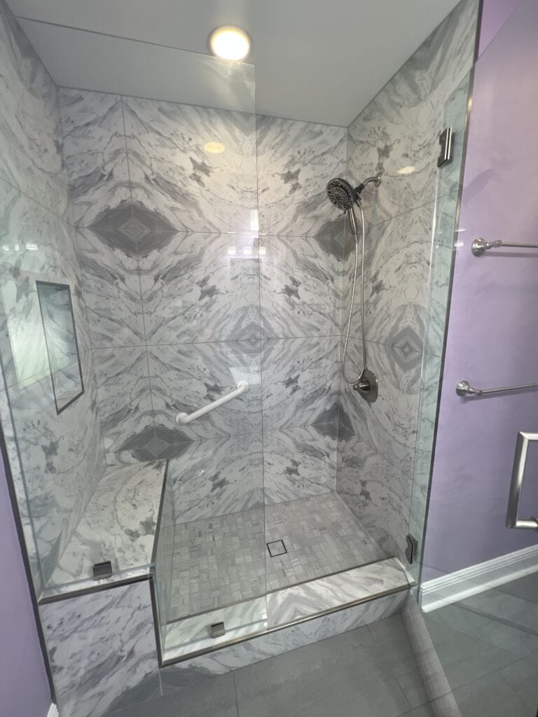 Custom walk-in shower with bookmatched marble tile, built-in bench, and recessed niche.