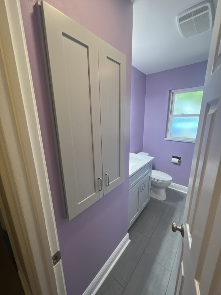 Lavender bathroom with gray floor tile, white upper cabinet, and compact vanity.
