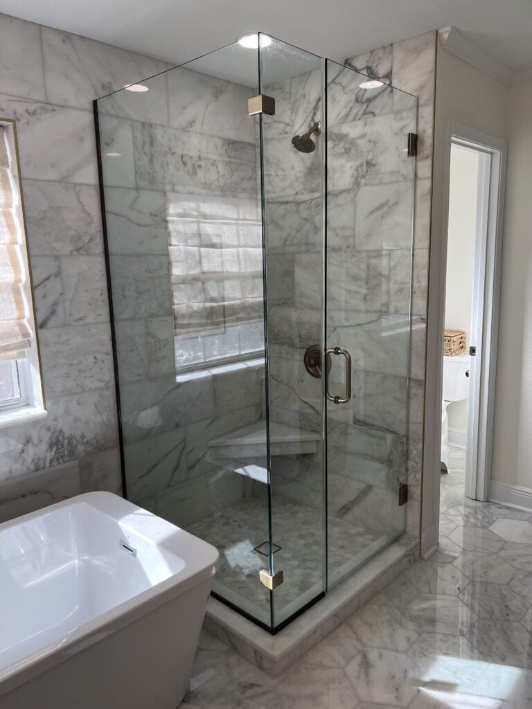 Marble shower with glass enclosure next to freestanding tub