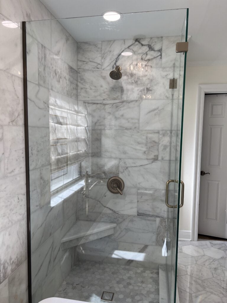Marble walk-in shower with hex tile floor and glass enclosure
