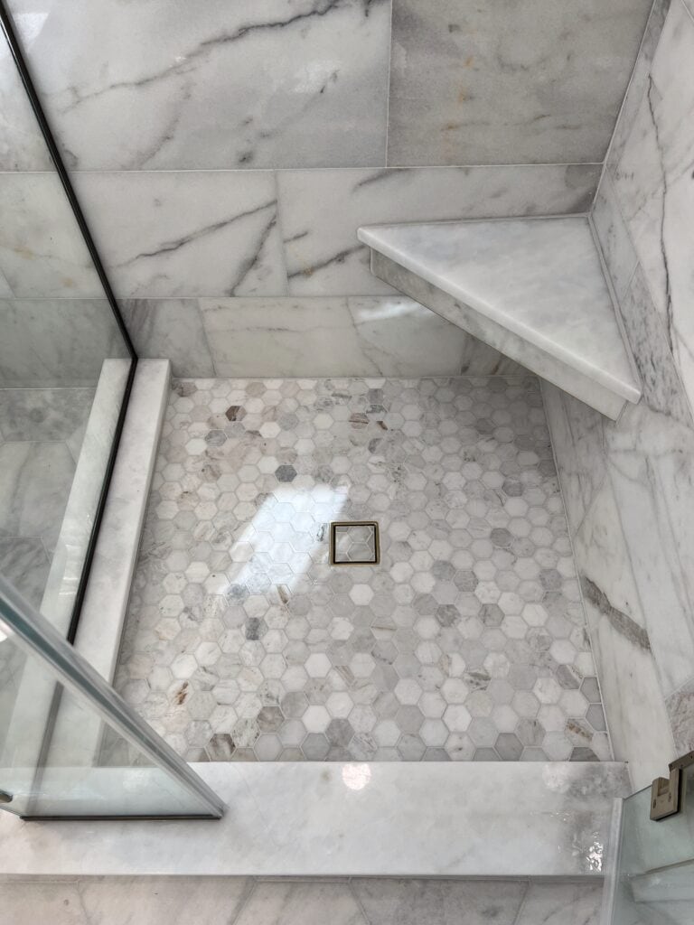 Hex tile shower floor with brass square drain and marble corner bench.