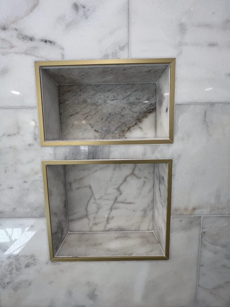 Close-up of dual marble shower niches with brass trim in a luxury bathroom remodel.