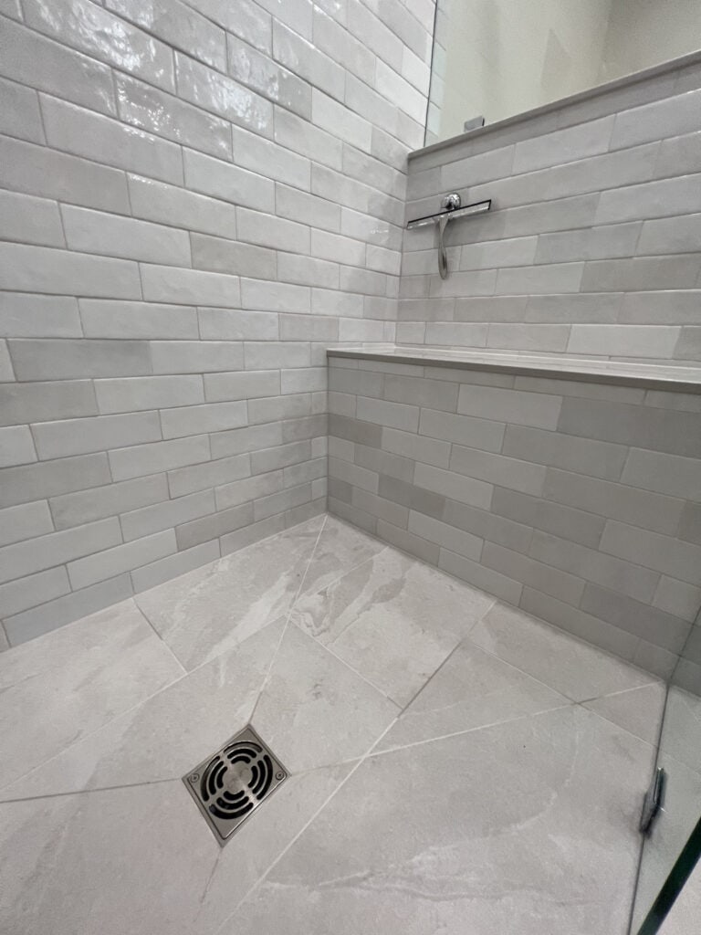 Close-up of custom tile cuts around linear shower drain and built-in bench